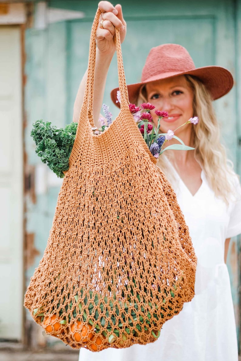 A blonde woman is holding a farmer's market bag full of vegetables, fruits, and a bunch of flowers.