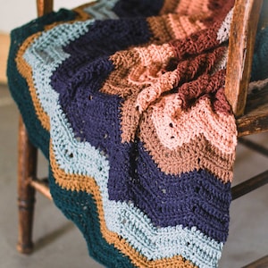 A colorful meditative zig zag stitch blanket draped on a wooden chair.