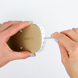 A woman poking through a hole on a slipper with a printable ruler attached using a pointed metal.