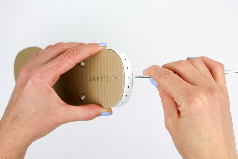 A woman poking through a hole on a slipper with a printable ruler attached using a pointed metal.