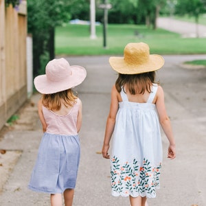 Two little girls are walking together wearing a matching summer hat in the colors pink and brown.