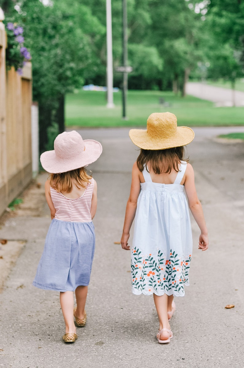 Two little girls are walking together wearing a matching summer hat in the colors pink and brown.
