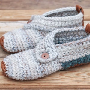A pair of white warm crochet slippers with leather soles and a button detail.