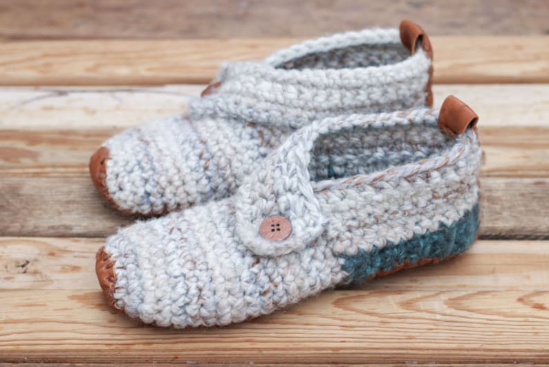 A pair of white warm crochet slippers with leather soles and a button detail.