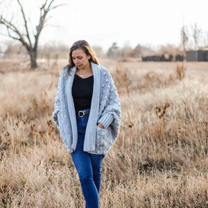 A chunky, rectangle cardigan worn by a woman standing on a field.