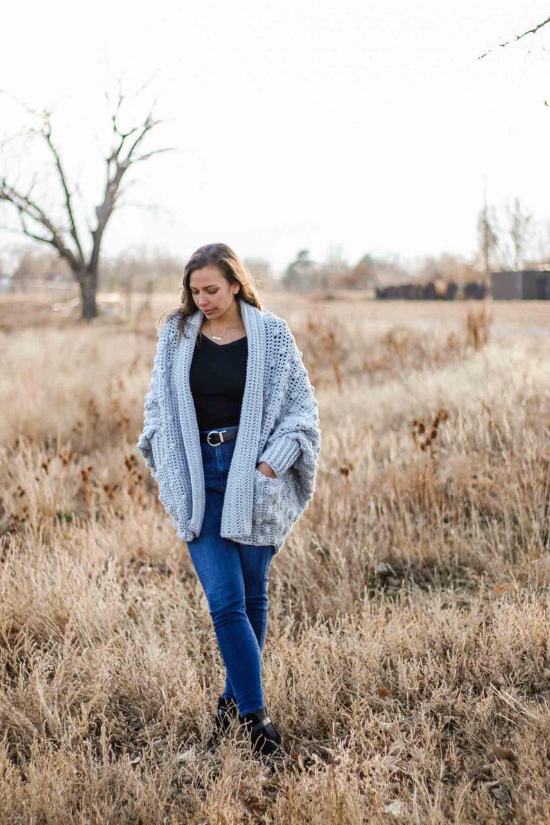 A chunky, rectangle cardigan worn by a woman standing on a field.