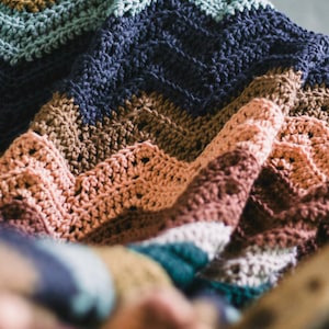 May include: A multi-colored crocheted blanket with stripes of teal, brown, blue, pink, and white.