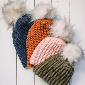 May include: Four crocheted winter hats with faux fur pom poms in navy blue, orange, pink, and olive green.