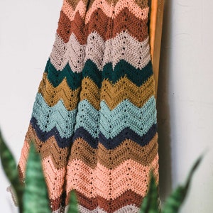 May include: A multi-colored crocheted blanket with a chevron pattern in shades of brown, pink, teal, green, and blue. The blanket is hanging on a wooden ladder.