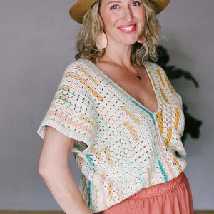 Blonde woman facing the camera wearing a crochet rectangle top, coral skirt, and a tan hat. Her hand is on her hip.