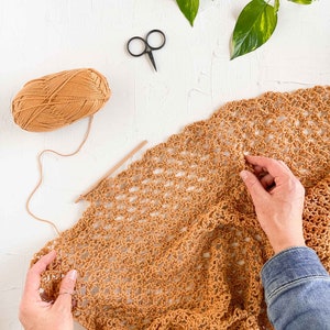 A woman is working on a cotton crochet bag using Solomon's knot stitch, a crochet hook, scissors, and a yarn skein.