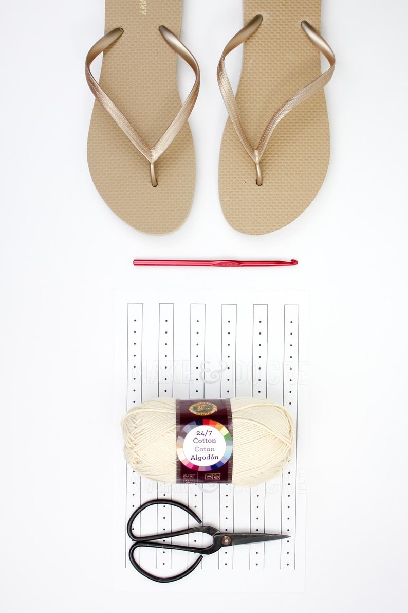A pair of beige slippers, a crochet hook, a yarn skein, a pair of scissors, and a printable ruler.