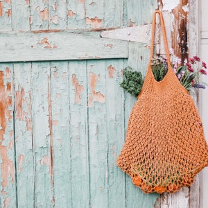 A mesh market bag full of vegetables, fruits, and flowers hanging on a green door's hinge.