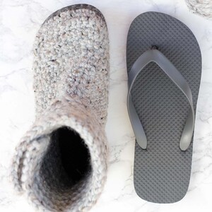 A crochet shoe with flip-flop soles, a gray flip-flop, a crochet hook, and a yarn skein.