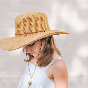 A little girl looking down wearing a brown wide brim fedora hat and a baby blue dress.