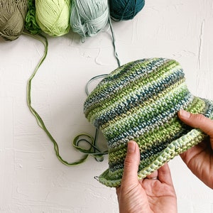 An in-progress green scrappy bucket hat with four yarn skeins.