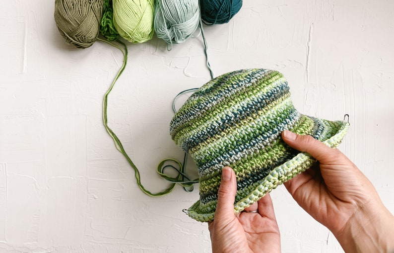An in-progress green scrappy bucket hat with four yarn skeins.