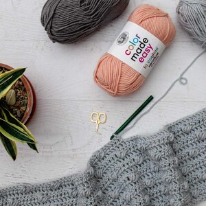 An in-progress bobble stitch pattern with a crochet hook, scissors, and three yarn skeins.