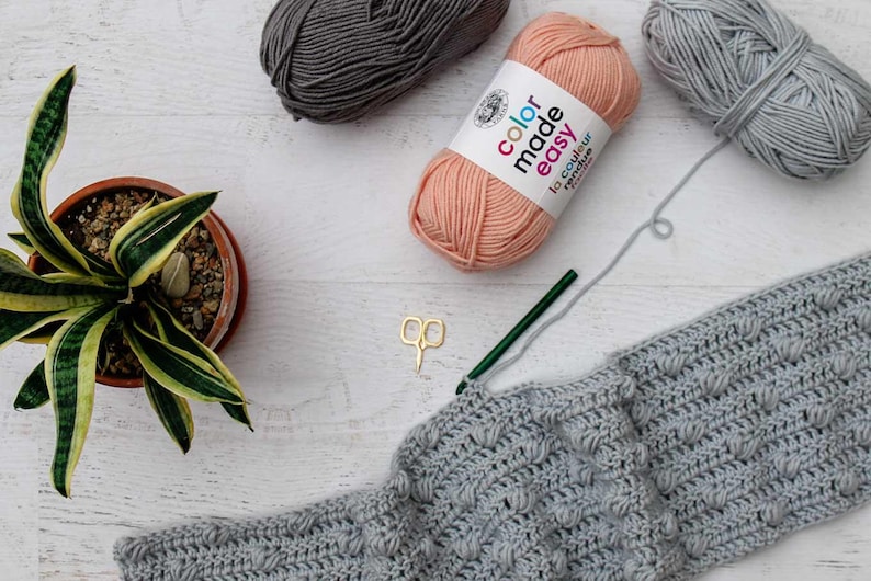 An in-progress bobble stitch pattern with a crochet hook, scissors, and three yarn skeins.