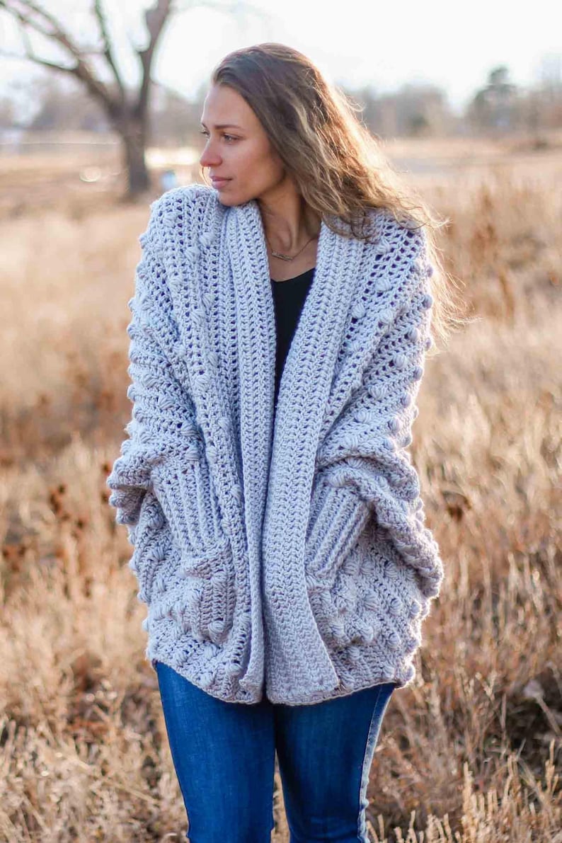 A chunky, rectangle cardigan worn by a woman standing on a field.