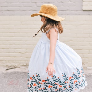 A little girl twirling around wearing a brown kids sun hat and a baby blue floral dress.
