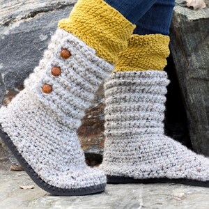 A woman standing on a rock wearing a pair of gray comfy sweater boots, yellow socks, and denim jeans.