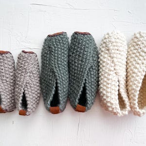 May include: Five pairs of knitted slippers in different colors. The slippers are made of a soft, textured yarn and have a pointed toe. The slippers are arranged in a row from left to right, with the smallest pair on the left and the largest pair on the right.