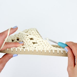A woman working on an in-progress boho summer slippers with a crochet hook.