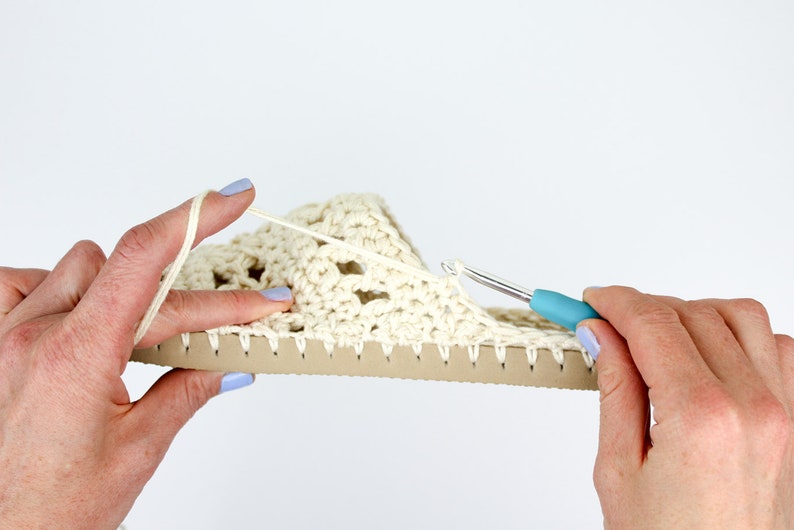 A woman working on an in-progress boho summer slippers with a crochet hook.
