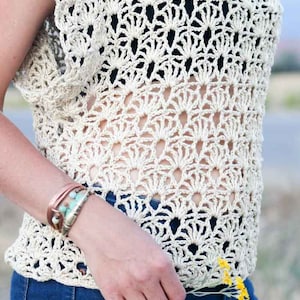 A woman wearing a boho crochet top with a black bandeau and denim jeans while holding a bunch of flowers.