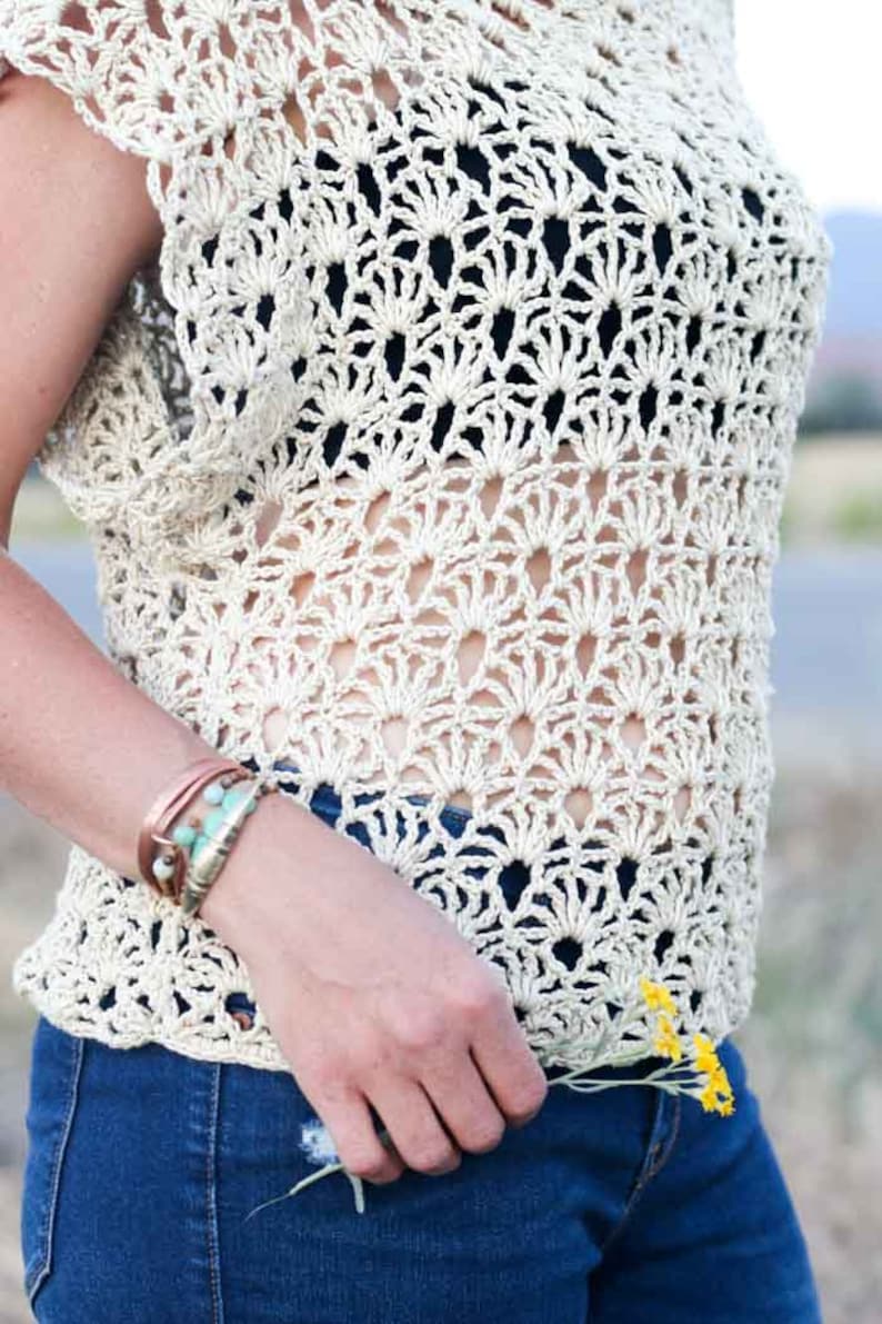 A woman wearing a boho crochet top with a black bandeau and denim jeans while holding a bunch of flowers.