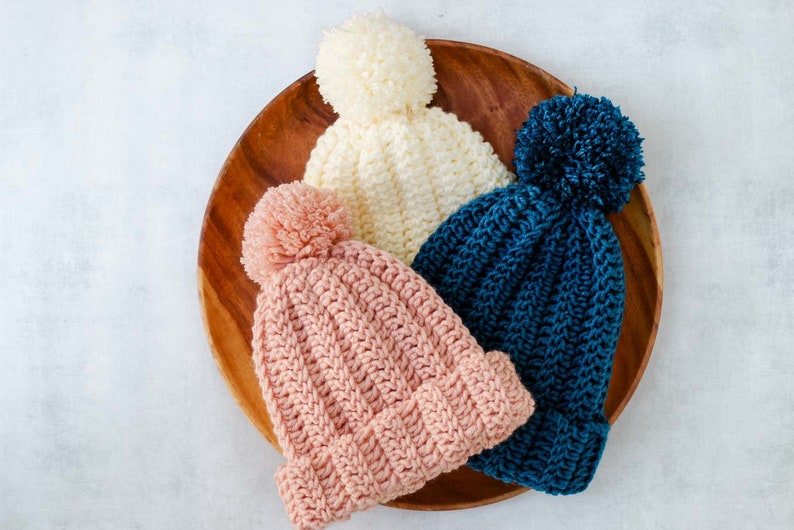 Three white, pink and blue easy adult beanies with pom poms.