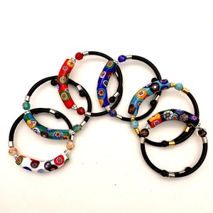 May include: Five colorful bracelets with black elastic bands and decorative glass beads. The bracelets feature a variety of colors and patterns, including red, blue, green, and yellow.