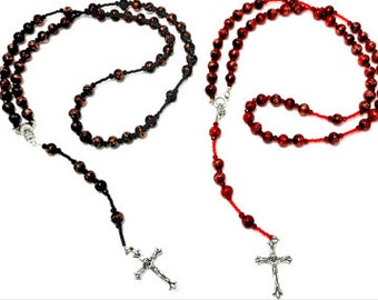 May include: Two rosaries featuring round beads with a marbled black and red pattern. One rosary is strung on black cord, and the other is strung on red cord. Both rosaries include a silver-toned metal crucifix pendant at the bottom end.