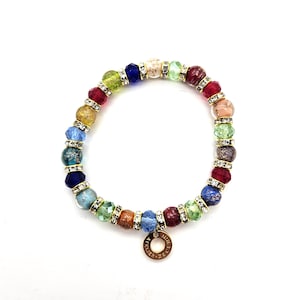 Op de afbeelding: Een veelkleurige kralenarmband met facetkralen in rood, groen, blauw, geel en bruin. Goudkleurige afstandhouders met heldere strass-steentjes scheiden de kralen. Een kleine goudkleurige bedel met tekst is bevestigd.