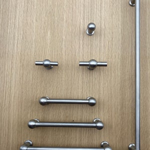 Może przedstawiać: Zestaw sześciu srebrnych uchwytów i gałek do szafek. Zestaw zawiera długi uchwyt prętowy, dwa krótsze uchwyty prętowe i trzy okrągłe gałki.