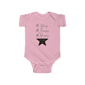 Pode incluir: Macac&atilde;o rosa para beb&ecirc; com uma lista de verifica&ccedil;&atilde;o preta que diz "Young, Scrappy, Hungry" e uma estrela dourada com o texto "Just Like My Country".