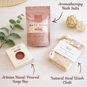May include: Aromatherapy bath set including a bath soak, artisan hand-poured soap bar, and natural sisal wash cloth. The bath soak is in a pink pouch, the soap bar in a beige box, and the wash cloth is beige.