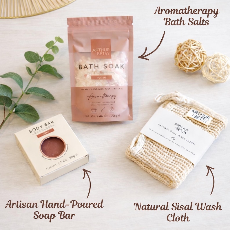 May include: Aromatherapy bath set including a bath soak, artisan hand-poured soap bar, and natural sisal wash cloth. The bath soak is in a pink pouch, the soap bar in a beige box, and the wash cloth is beige.