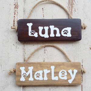 Pode incluir: Dois letreiros de madeira para c&atilde;es com pegadas de patas. O letreiro de cima &eacute; castanho escuro com o nome "Luna" e o letreiro de baixo &eacute; castanho claro com o nome "Marley".
