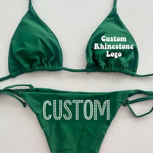 May include: Green bikini with a custom rhinestone logo that says "Custom Rhinestone Logo" on the top and "CUSTOM" on the bottom.