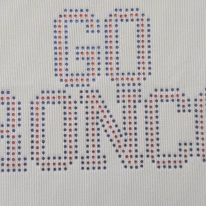 K&ouml;nnte beinhalten: Wei&szlig;er Stoff mit den Worten "GO BRONCOS" aus blauen und roten Strasssteinen. Der Text ist zentriert, die Strasssteine sind gleichm&auml;&szlig;ig angeordnet und erzeugen einen Glanzeffekt.