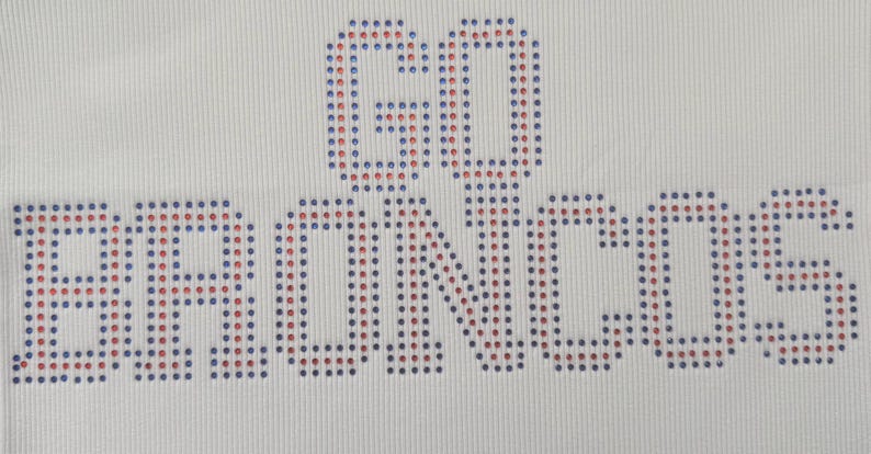K&ouml;nnte beinhalten: Wei&szlig;er Stoff mit den Worten "GO BRONCOS" aus blauen und roten Strasssteinen. Der Text ist zentriert, die Strasssteine sind gleichm&auml;&szlig;ig angeordnet und erzeugen einen Glanzeffekt.
