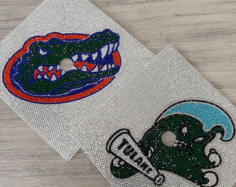 May include: Two silver rhinestone coasters. One features a green and blue alligator head with an orange and blue outline. The other coaster has a green creature with a blue wave and a megaphone that says "TULANE".