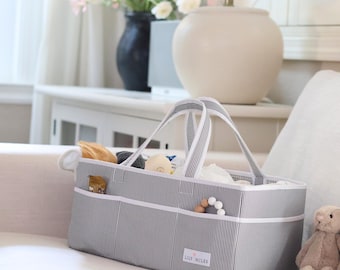 May include: A rectangular grey and white pinstriped storage caddy with two fabric handles and multiple exterior pockets. The front features a white label with the text Lily Miles. The interior contains various small items and toys.