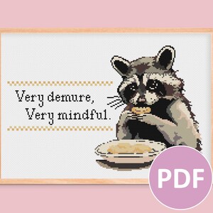 May include: Cross-stitch pattern featuring a raccoon eating a cookie with the text "Very demure, Very mindful." in a white frame.