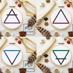 May include: Four different cross-stitch patterns featuring the four elements: air, fire, water, and earth. Each pattern is displayed in a wooden embroidery hoop on a white background. The patterns are in shades of purple, red, blue, and green.
