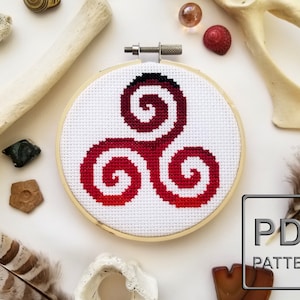 May include: A red and white cross-stitch embroidery hoop with a red triple spiral design. The hoop is on a white surface with various decorative items around it. The text "PDF PATTERN" is visible in the lower right corner of the image.