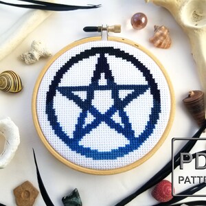 May include: A blue and black pentagram cross stitch pattern in a wooden embroidery hoop. The pattern is a gradient from black to blue. The hoop is on a white background with various decorative items.