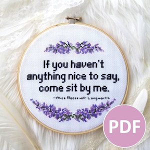 May include: A white embroidery hoop with a cross-stitch design featuring a quote by Alice Roosevelt Longworth: "If you haven't anything nice to say, come sit by me." The design includes purple flowers and a white background.